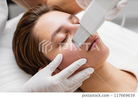 Female receiving a facial treatment with a handheld device in a spa during the day Female receiving a facial treatment with a handheld device in a spa during the day 117669639