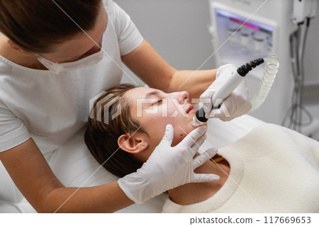 Skincare professional performing microneedling on a client in a modern clinic Skincare professional performing microneedling on a client in a modern clinic 117669653