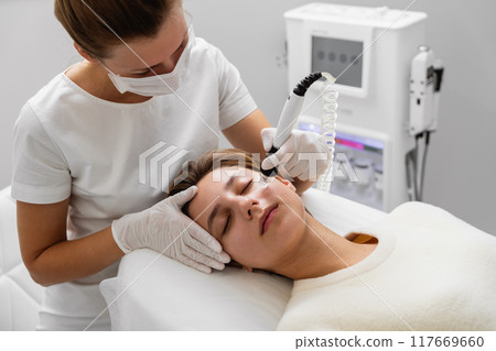 Skincare specialist performing facial treatment on a client in a modern clinic 117669660
