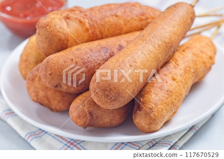 Heap of corn dogs on white plate, served with ketchup, horizontal Heap of corn dogs on white plate, served with ketchup, horizontal 117670529