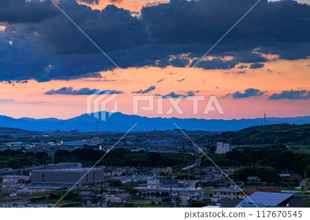 Evening view from Shiroyamadai, Kizugawa City, the southernmost part of Kyoto Prefecture. Dark clouds above the sunset and a JR Nara Line train crossing the Kizugawa River iron bridge #8 117670545