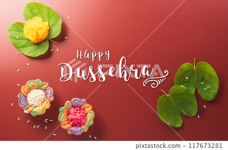 Happy Dussehra. Yellow flowers, green leaf and rice on dark paper background. Dussehra Indian Festival concept. 117673281