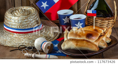 Chilean independence day concept. fiestas patrias. Tipical baked empanadas de pino, wine or chicha, hat and play emboque. Dish and drink on 18 September party, wooden background Chilean independence day concept. fiestas patrias. Tipical baked empanadas de pino, wine or chicha, hat and play emboque. Dish and drink on 18 September party, wooden background 117673426