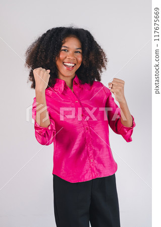 Joyful African American woman celebrating success with raised fists, expressing excitement and happiness. Joyful African American woman celebrating success with raised fists, expressing excitement and happiness. 117675669
