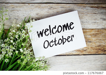 Welcome October text on paper card with flowers frame top view on wooden background 117676867