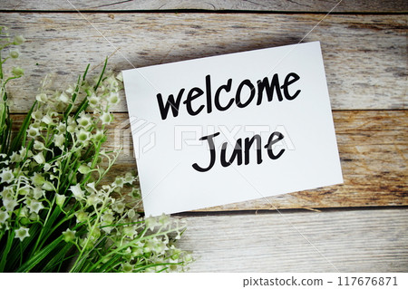 Welcome June text on paper card with flowers frame top view on wooden background Welcome June text on paper card with flowers frame top view on wooden background 117676871