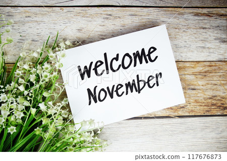 Welcome November text on paper card with flowers frame top view on wooden background 117676873