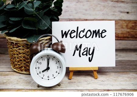 Welcome May text on paper card with alarm clock on wooden background 117676906