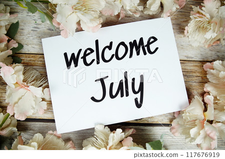 Welcome July text on paper card with flowers frame top view on wooden background Welcome July text on paper card with flowers frame top view on wooden background 117676919