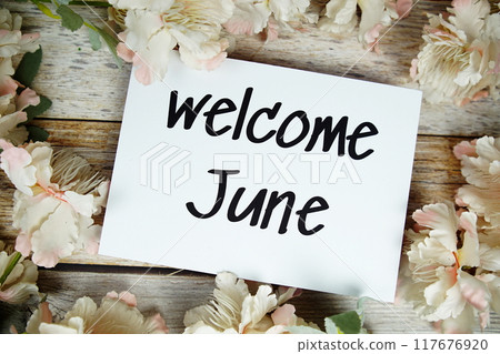 Welcome June text on paper card with flowers frame top view on wooden background Welcome June text on paper card with flowers frame top view on wooden background 117676920