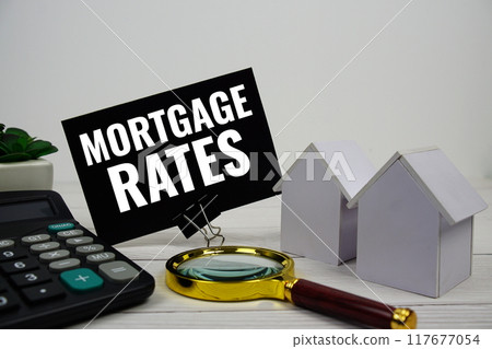 Mortgage Rates text message with house model, calculator and magnifying glass on wooden background 117677054