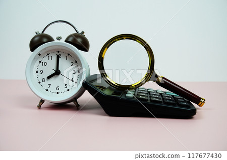 Magnifiying glass with alarm clock and calculator on pink background 117677430