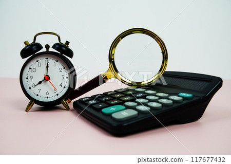 Magnifiying glass with alarm clock and calculator on pink background 117677432