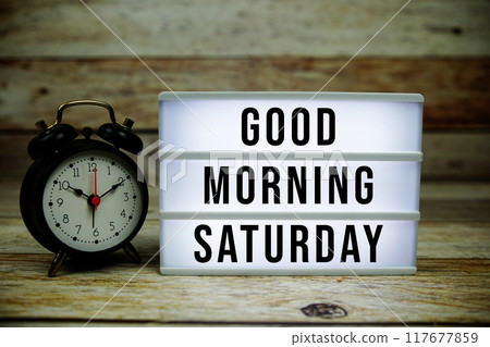Good Morning Saturday text on LED lightbox with alarm clock on wooden background 117677859