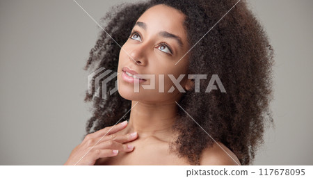 Beauty and healthcare - beautiful African American woman with curly afro hairstyle and clean, healthy skin touching her face, neck, shoulders, looking at the camera with a calm look and a slight smile Beauty and healthcare - beautiful African American woman with curly afro hairstyle and clean, healthy skin touching her face, neck, shoulders, looking at the camera with a calm look and a slight smile 117678095