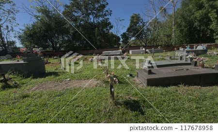 Walking alongside graves in a serene cemetery with lush green grass 117678958