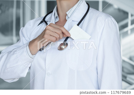 A doctor in a white coat takes a business card out of his pocket. 117679689