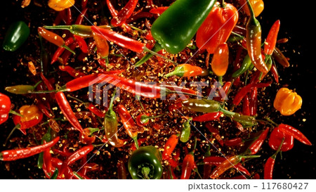 Group of coloured chilli peppers flying on black background. 117680427