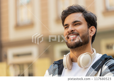 Smiling Indian young man smiling at camera, resting, relaxation feel satisfied in city street 117680523