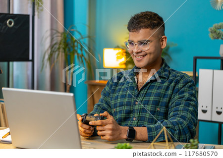 Excited Indian man playing video game on laptop computer spending leisure time at home office Excited Indian man playing video game on laptop computer spending leisure time at home office 117680570