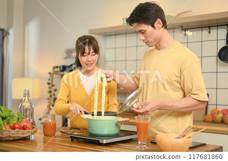 Cheerful young couple cooking together at kitchen counter. People, food and domestic kitchen concept Cheerful young couple cooking together at kitchen counter. People, food and domestic kitchen concept 117681860