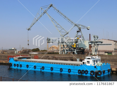 An old mechanical crane made in 1968 loading steel pipes onto a barge in a corner of the port. 117681867