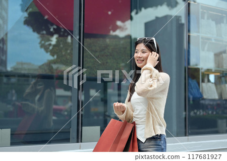Cheerful asian woman carrying shopping bags walking in the city street Cheerful asian woman carrying shopping bags walking in the city street 117681927