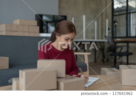 woman, online seller, using a notebook efficiently manages customer orders and delivery through the e-commerce platform 117681962