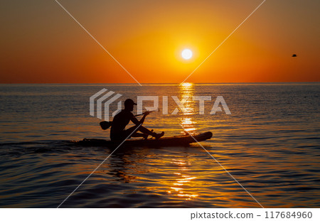 Silhouette of a man floating on a board with an oar. Dawn sun on the sea. Swimming on a supboard. Water active sports. Beautiful landscape. Sunset on the sea. Ocean coast. Copy space. 117684960