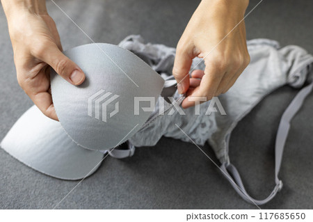 Woman puts pads in a bra. Grey colour cotton lingerie. 117685650