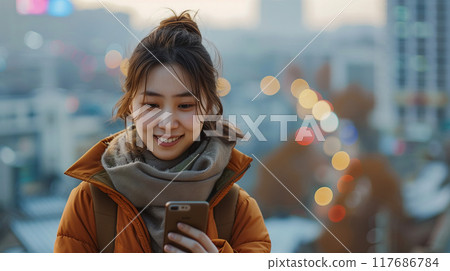 Asian woman, Her body language suggests comfort and ease, looking at her phone 117686784