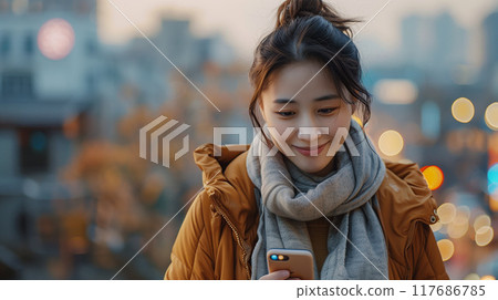 Asian woman's smile radiates warmth and positivity, looking at her phone 117686785