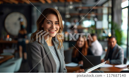 A confident businesswoman stands and smiles, holding a tablet 117687140