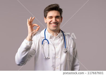 Doctor showing OK sign, white clinic studio background. Handsome doc man smiling Doctor showing OK sign, white clinic studio background. Handsome doc man smiling 117687601