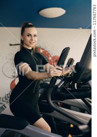 Young woman exercising on elliptical machine in a modern fitness center 117687763
