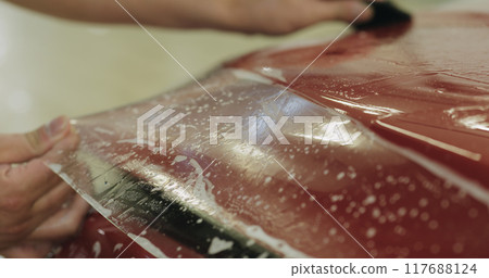 professional applying protective film to the red car 117688124