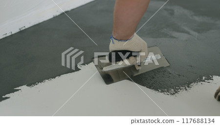 closeup male worker applying micro concrete plaster coating on the floor with a trowel closeup male worker applying micro concrete plaster coating on the floor with a trowel 117688134