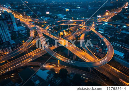 Aerial view of a highway intersection at night showing traffic flow on the roads, with a city background. Cars at a big crossroads at night. Urban landscape Aerial view of a highway intersection at night showing traffic flow on the roads, with a city background. Cars at a big crossroads at night. Urban landscape 117688644
