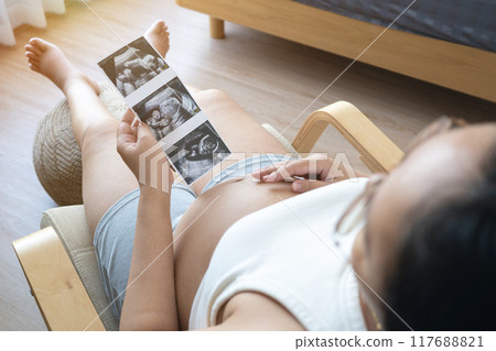 pregnant woman holds an ultrasound photo of her baby, smiling as she gazes at the image. The ultrasound shows a clear picture of the developing baby, capturing a precious moment of motherhood pregnant woman holds an ultrasound photo of her baby, smiling as she gazes at the image. The ultrasound shows a clear picture of the developing baby, capturing a precious moment of motherhood 117688821
