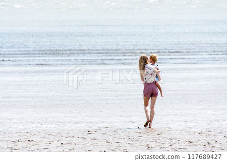 A blonde mother and her child walking along a shallow sandy beach on the outskirts of South Wales A blonde mother and her child walking along a shallow sandy beach on the outskirts of South Wales 117689427