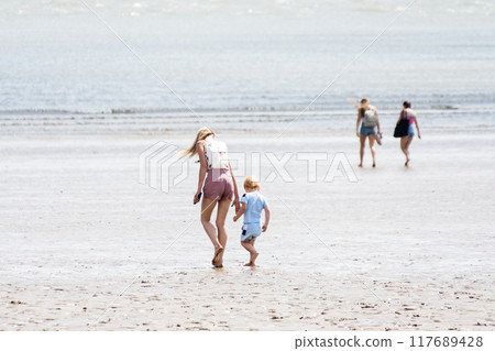 A blonde mother and her child walking along a shallow sandy beach on the outskirts of South Wales A blonde mother and her child walking along a shallow sandy beach on the outskirts of South Wales 117689428