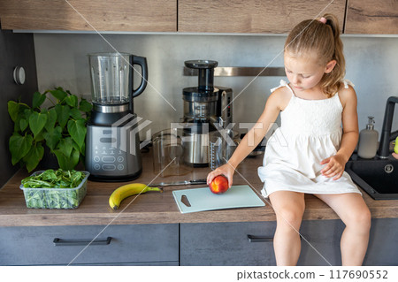 Little girl preparing a healthy juice or smoothie with fresh fruits in home kitchen 117690552