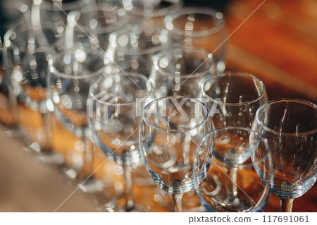 A close-up view of multiple empty wine glasses arranged in rows on a wooden table. 117691061