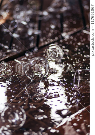 Close up of broken wine glasses and spilled wine, parts of the broken glass on floor with water splash on wooden terrace 117691067