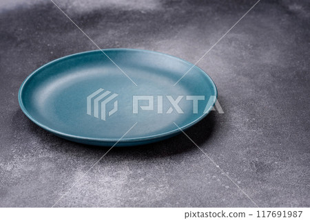 Empty ceramic plate on a dark textured background Empty ceramic plate on a dark textured background 117691987
