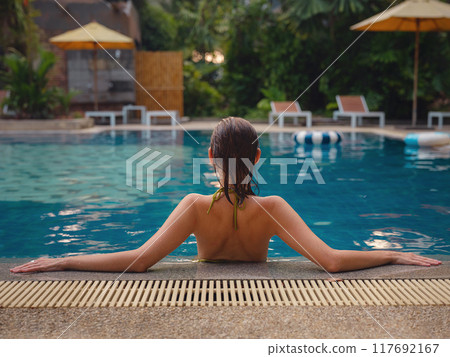 Vacation lifestyle scene of young woman sitting in swimming pool 117692167