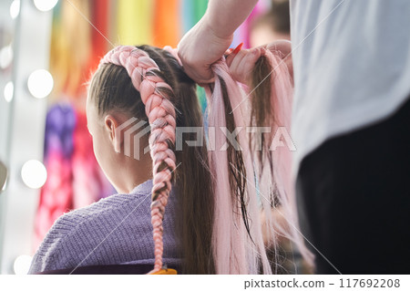 The hands of the master who weave the kanekalon material into the hair. The master braids the child's pigtails from a pink kanekalon. Rear view with copy space. High quality photo The hands of the master who weave the kanekalon material into the hair. The master braids the child's pigtails from a pink kanekalon. Rear view with copy space. High quality photo 117692208