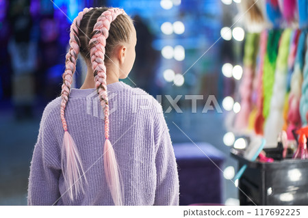 An unrecognizable girl with pigtails made of pink kanekalon. The girl looks at herself in the mirror and is delighted with her new hairstyle from the kanekalon in the beauty salon. High quality photo An unrecognizable girl with pigtails made of pink kanekalon. The girl looks at herself in the mirror and is delighted with her new hairstyle from the kanekalon in the beauty salon. High quality photo 117692225