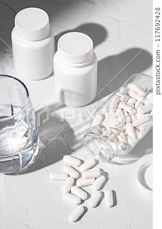 Food supplement concept. Bottles with capsules of probiotics, vitamins, white pills and a glass of water 117692428