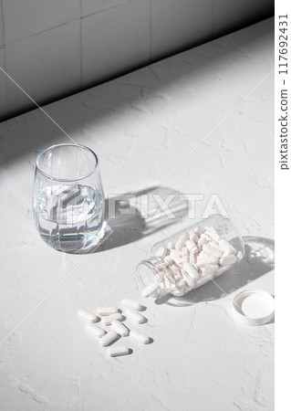 Food supplement concept. clear bottle with capsules of probiotics, vitamins, white pills and a glass of water Food supplement concept. clear bottle with capsules of probiotics, vitamins, white pills and a glass of water 117692431